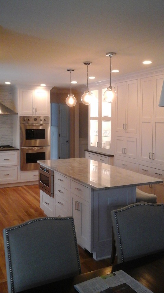 Example of a mid-sized transitional l-shaped light wood floor eat-in kitchen design in Newark with a double-bowl sink, shaker cabinets, white cabinets, solid surface countertops, multicolored backsplash, stone tile backsplash, stainless steel appliances and an island