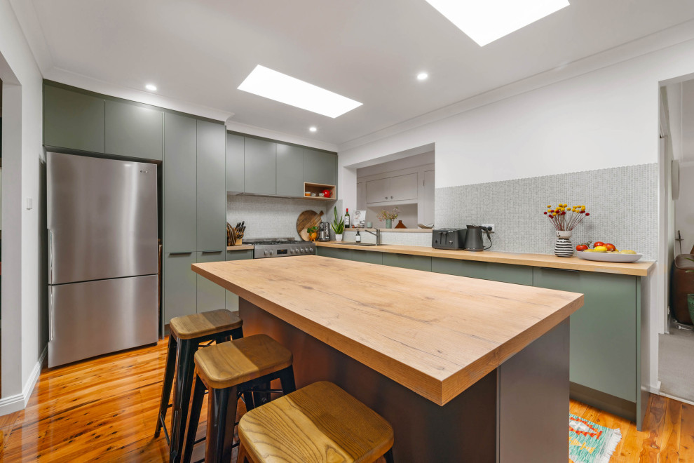 Inspiration for a mid-sized contemporary l-shaped kitchen pantry in Sydney with a drop-in sink, flat-panel cabinets, green cabinets, wood benchtops, grey splashback, cement tile splashback, stainless steel appliances, light hardwood floors, with island and brown benchtop.