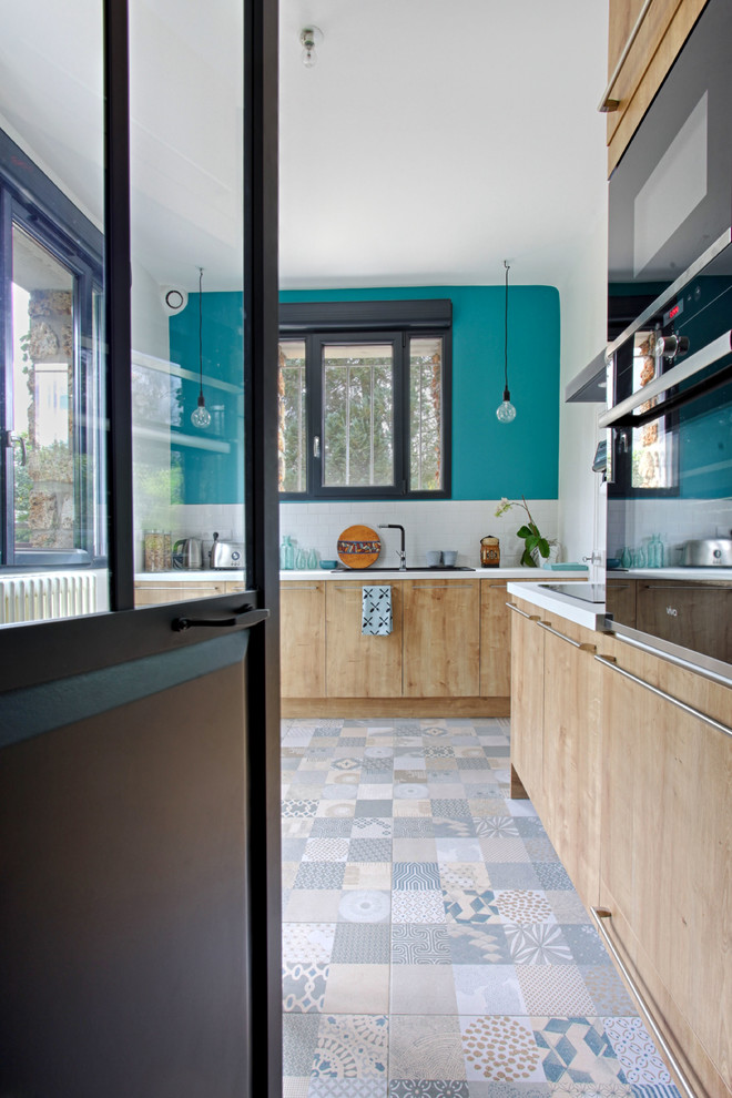 Enclosed kitchen - mid-sized scandinavian l-shaped ceramic tile and multicolored floor enclosed kitchen idea in Marseille with a drop-in sink, flat-panel cabinets, light wood cabinets, laminate countertops, white backsplash, ceramic backsplash, black appliances and no island