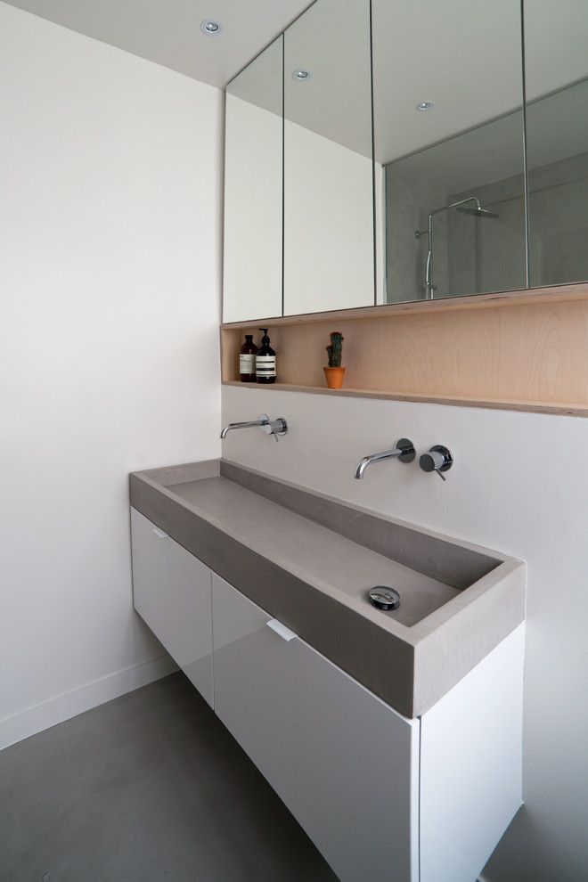 Inspiration for a mid-sized 3/4 bathroom in Paris with beaded inset cabinets, white cabinets, a curbless shower, a wall-mount toilet, gray tile, white walls, concrete floors, a trough sink, concrete benchtops, grey floor, a hinged shower door, grey benchtops, a niche, a double vanity and a floating vanity.