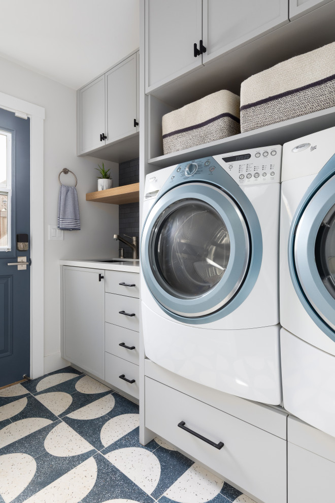 Dedicated laundry room - mid-sized contemporary galley concrete floor and multicolored floor dedicated laundry room idea in San Francisco with an undermount sink, raised-panel cabinets, gray cabinets, quartz countertops, blue backsplash, ceramic backsplash, gray walls, a side-by-side washer/dryer and white countertops