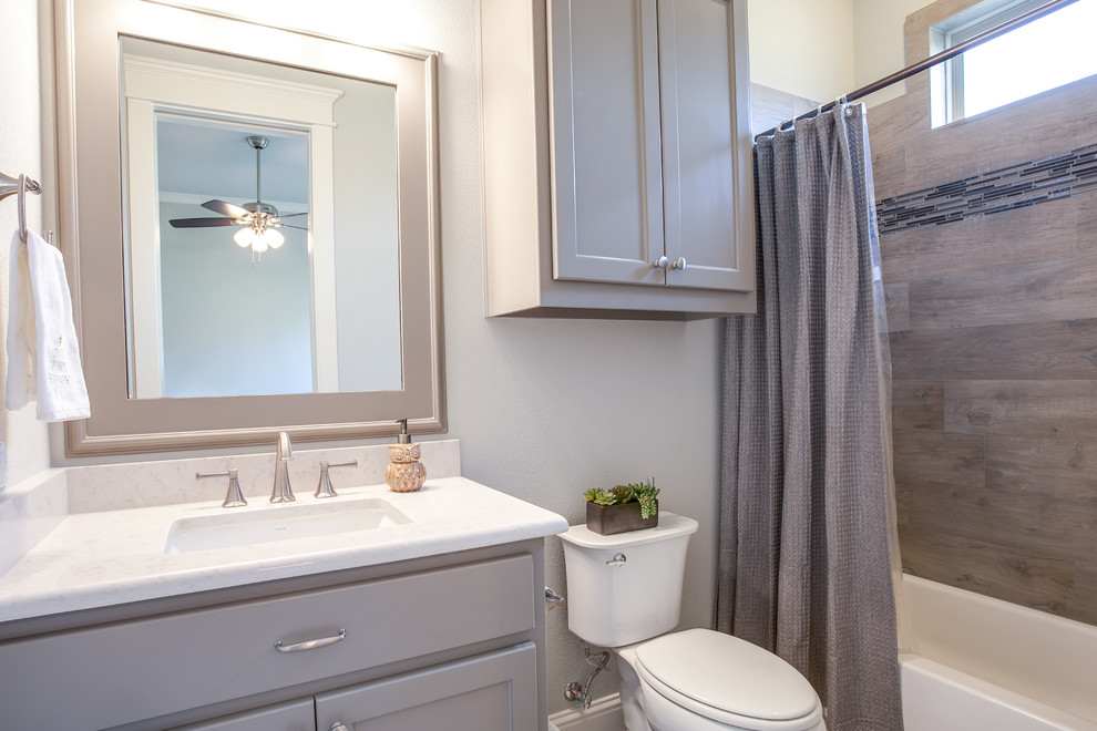 This is an example of a mid-sized country bathroom in Dallas with shaker cabinets, grey cabinets, a shower/bathtub combo, gray tile, grey walls, ceramic floors, an undermount sink, marble benchtops, a two-piece toilet and ceramic tile.