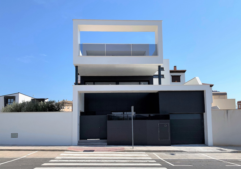 Mid-sized minimalist white three-story stucco exterior home photo in Other