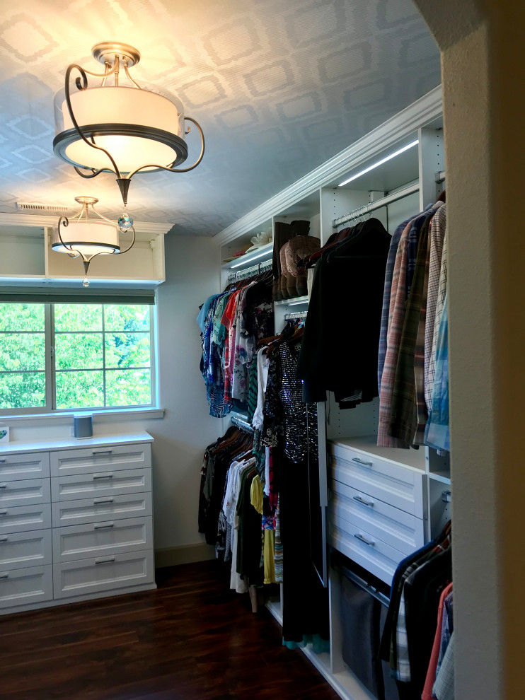 This is an example of a mid-sized transitional gender-neutral walk-in wardrobe in Portland with white cabinets, dark hardwood floors, brown floor and wallpaper.