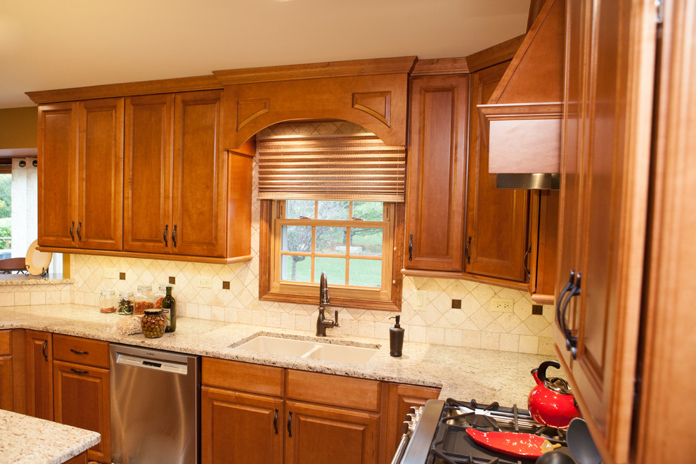 Photo of a mid-sized traditional u-shaped open plan kitchen in Chicago with raised-panel cabinets, granite benchtops, light hardwood floors, with island, an undermount sink, light wood cabinets, beige splashback, stone tile splashback and stainless steel appliances.