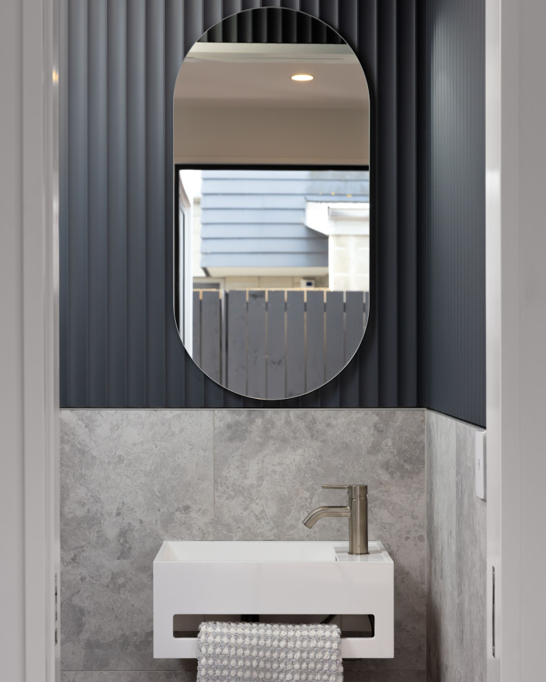 Photo of a small contemporary cloakroom in Christchurch with a wall mounted toilet, grey tiles, ceramic tiles, blue walls, laminate floors, a wall-mounted sink, brown floors, a freestanding vanity unit and wainscoting.