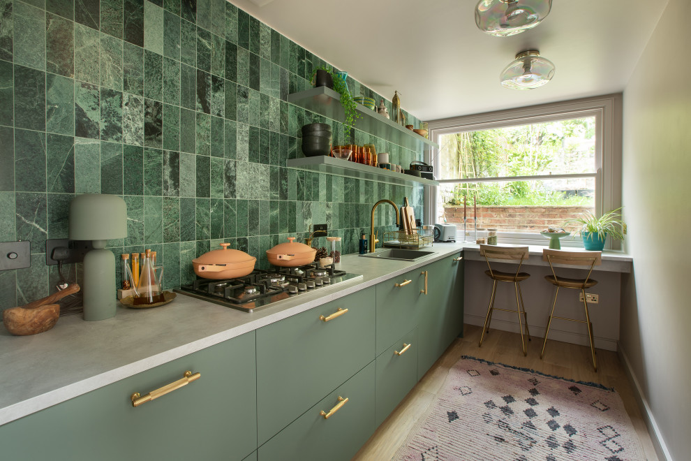 Inspiration for a mid-sized contemporary galley open plan kitchen in London with an integrated sink, flat-panel cabinets, green cabinets, solid surface benchtops, green splashback, marble splashback, stainless steel appliances, medium hardwood floors and white benchtop.