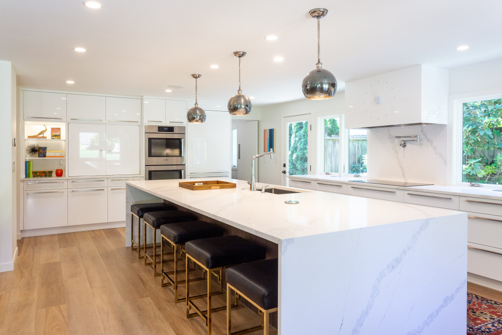 Large contemporary single-wall eat-in kitchen in Seattle with an undermount sink, flat-panel cabinets, white cabinets, quartzite benchtops, white splashback, stone slab splashback, panelled appliances, light hardwood floors, with island, brown floor and white benchtop.