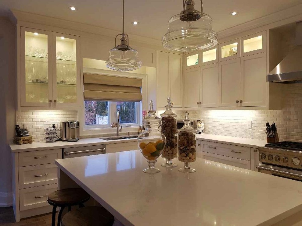 Example of a mid-sized transitional l-shaped medium tone wood floor and brown floor open concept kitchen design in Toronto with an undermount sink, beaded inset cabinets, white cabinets, solid surface countertops, white backsplash, brick backsplash, stainless steel appliances, an island and white countertops