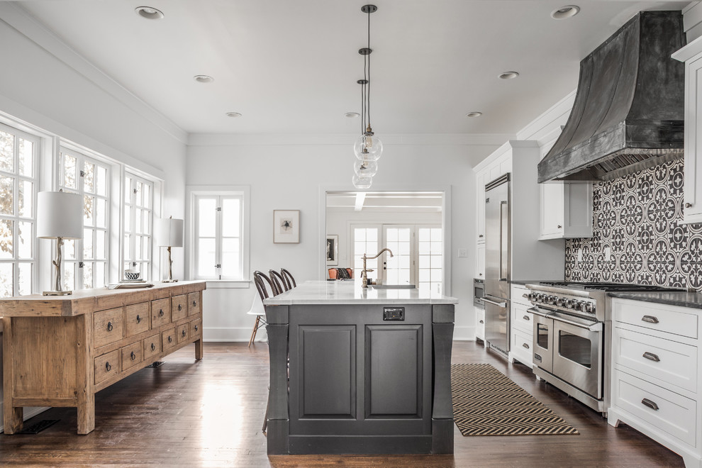 Design ideas for a traditional galley kitchen in Indianapolis with a farmhouse sink, shaker cabinets, white cabinets, black splashback, cement tile splashback, stainless steel appliances, dark hardwood floors, with island and brown floor.