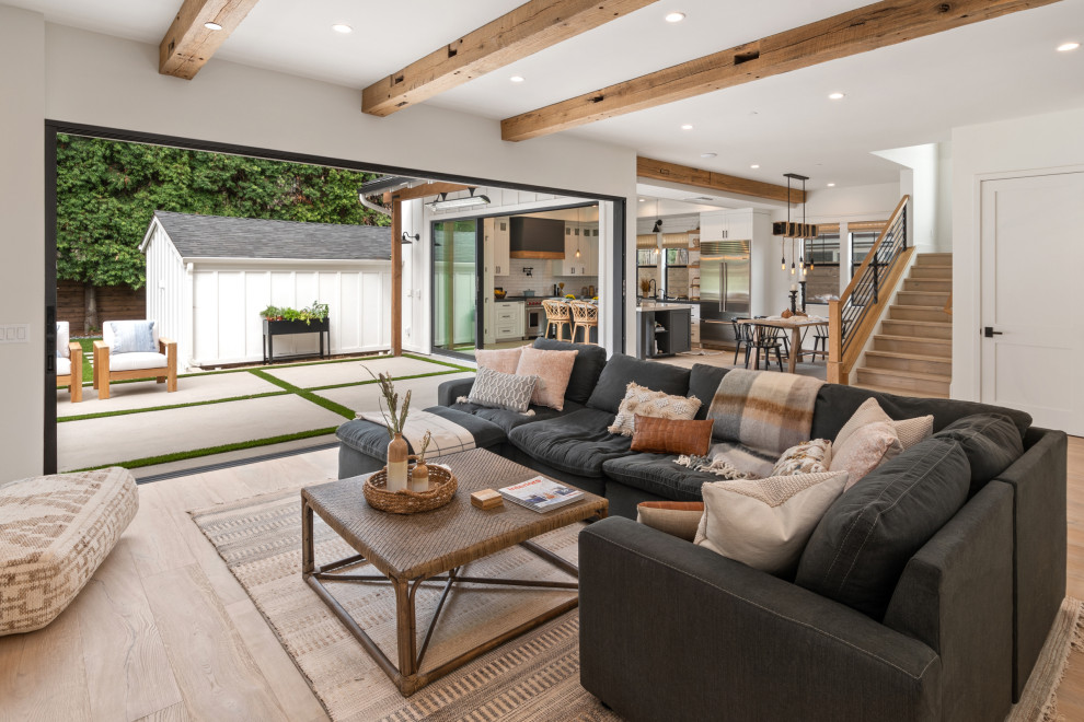 Design ideas for a large farmhouse open plan living room in San Diego with white walls, light hardwood flooring and exposed beams.