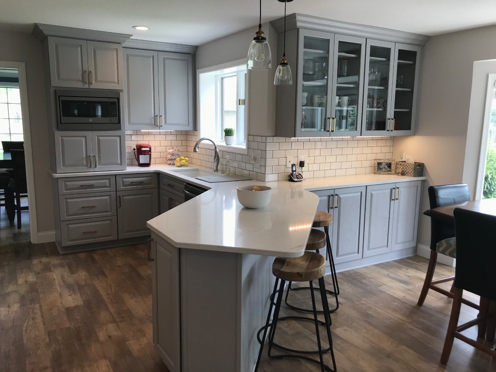 Inspiration for a mid-sized transitional u-shaped vinyl floor and brown floor enclosed kitchen remodel with an undermount sink, raised-panel cabinets, gray cabinets, quartz countertops, white backsplash, ceramic backsplash, a peninsula and white countertops