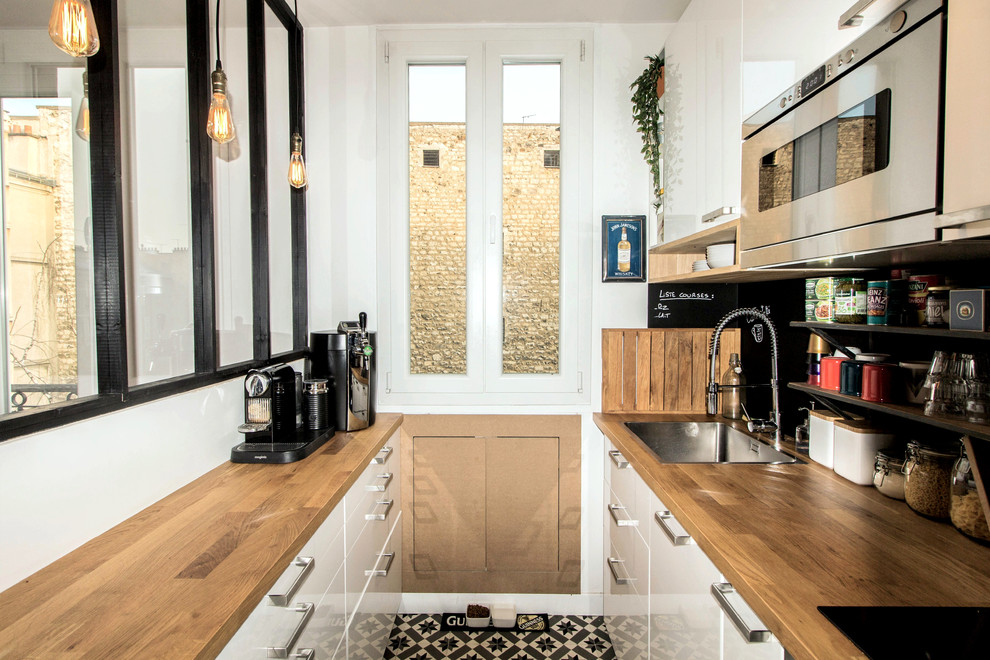 Inspiration for a small industrial galley open plan kitchen in Paris with an undermount sink, flat-panel cabinets, white cabinets, wood benchtops, black splashback, slate splashback, panelled appliances, cement tiles and no island.