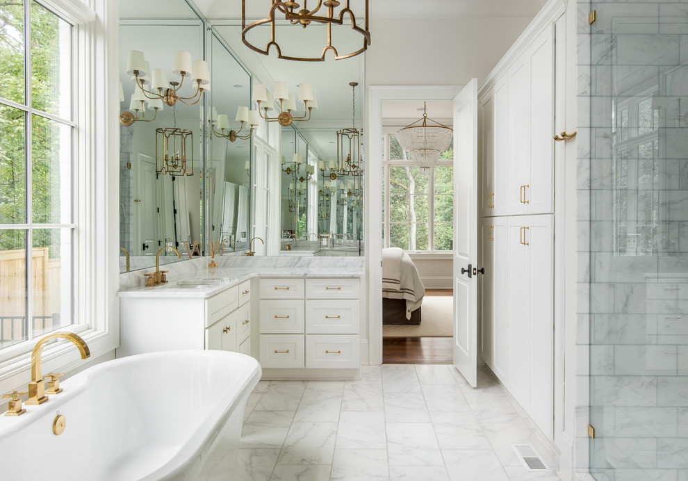 Photo of a mid-sized transitional master bathroom in Nashville with shaker cabinets, white cabinets, a freestanding tub, an alcove shower, white tile, marble, white walls, porcelain floors, an undermount sink, marble benchtops, white floor, a hinged shower door and white benchtops.