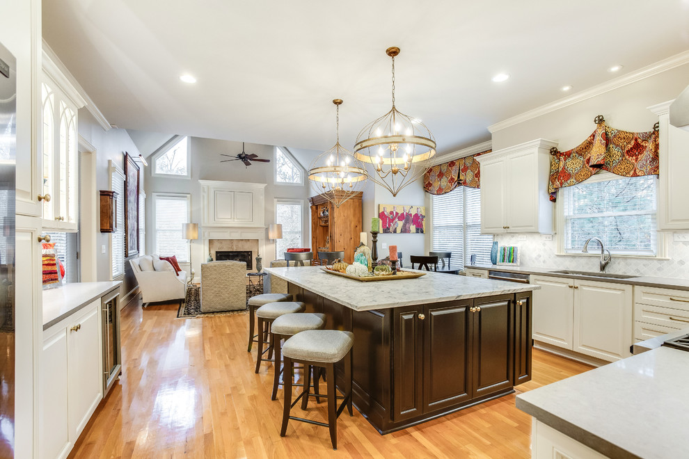 Example of a large transitional u-shaped light wood floor and yellow floor open concept kitchen design in Birmingham with raised-panel cabinets, white cabinets, marble countertops, white backsplash, marble backsplash, stainless steel appliances, an island and white countertops