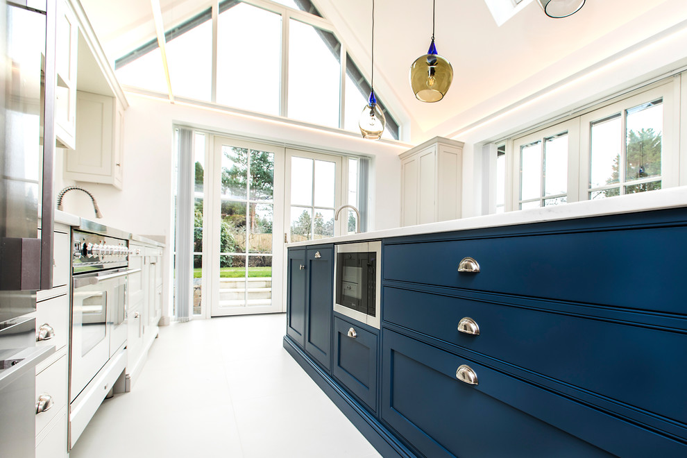 This is an example of a large traditional single-wall open plan kitchen in Hampshire with a double-bowl sink, shaker cabinets, blue cabinets, quartzite benchtops, white splashback, stone slab splashback, stainless steel appliances, ceramic floors, with island, white floor and white benchtop.