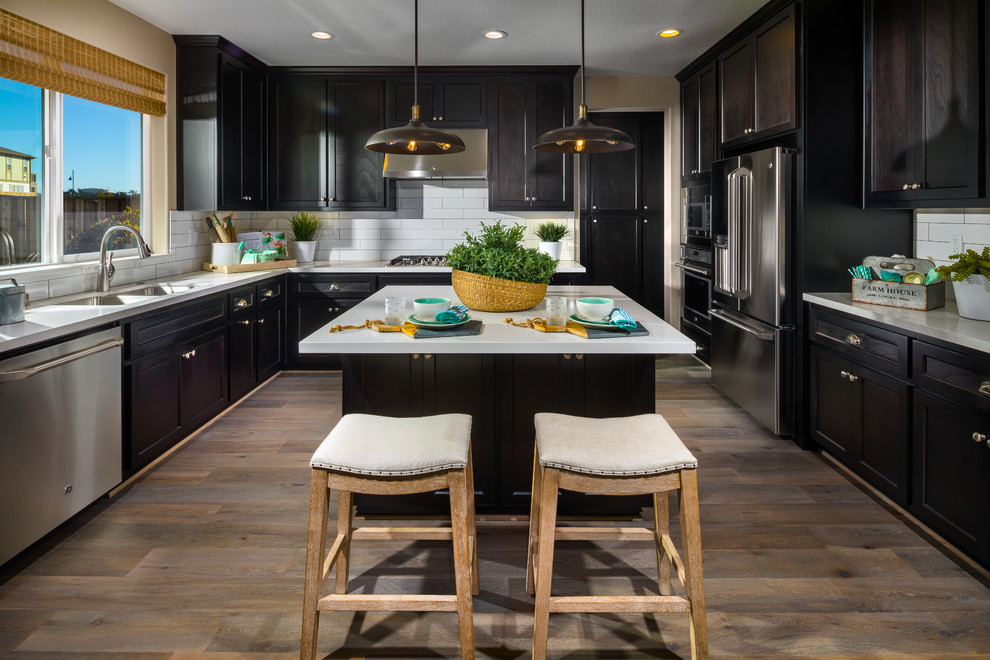 Transitional kitchen in San Francisco with a double-bowl sink, shaker cabinets, black cabinets, white splashback, stainless steel appliances, medium hardwood floors, with island and white benchtop.