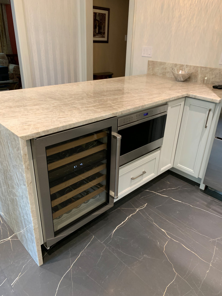This is an example of a mid-sized transitional l-shaped separate kitchen in New York with an undermount sink, flat-panel cabinets, grey cabinets, quartzite benchtops, beige splashback, stone slab splashback, stainless steel appliances, marble floors, a peninsula, black floor and beige benchtop.