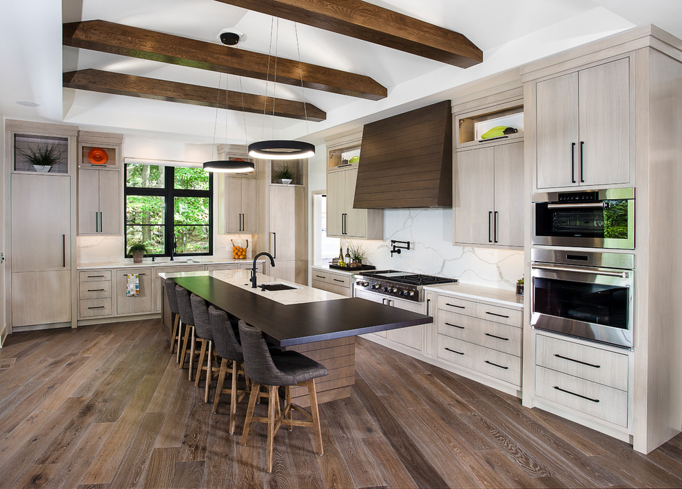 Design ideas for an expansive modern l-shaped open plan kitchen in Grand Rapids with an undermount sink, flat-panel cabinets, light wood cabinets, white splashback, marble splashback, stainless steel appliances, with island, brown floor, quartzite benchtops, dark hardwood floors and white benchtop.