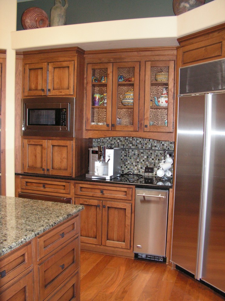 This is an example of a traditional kitchen in Phoenix with glass-front cabinets, medium wood cabinets, stainless steel appliances and with island.