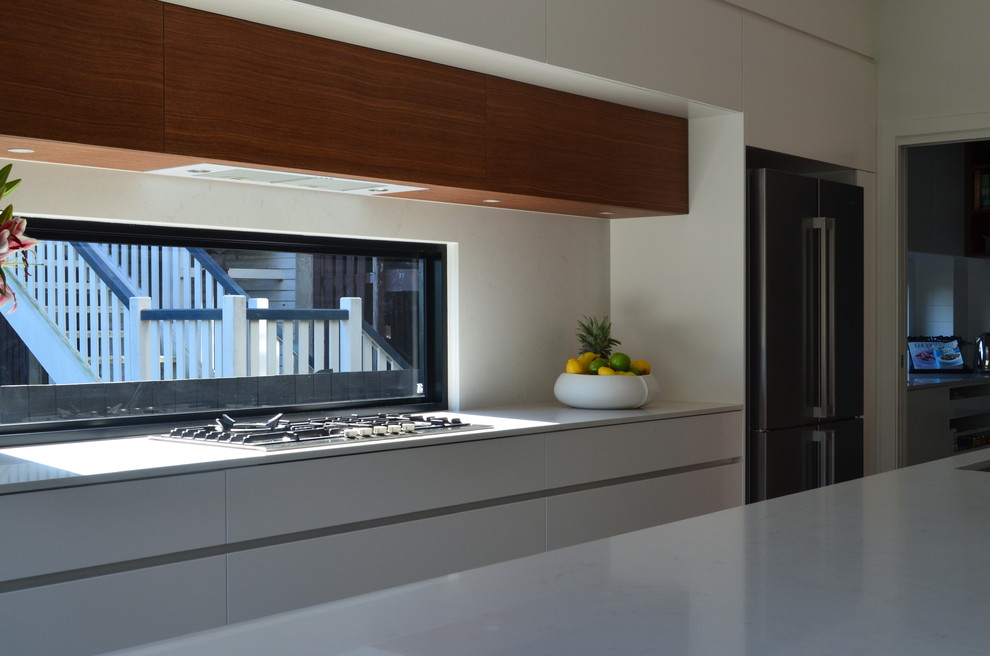 Photo of a contemporary l-shaped open plan kitchen in Brisbane with an undermount sink, flat-panel cabinets, white cabinets, solid surface benchtops, white splashback, window splashback and stainless steel appliances.