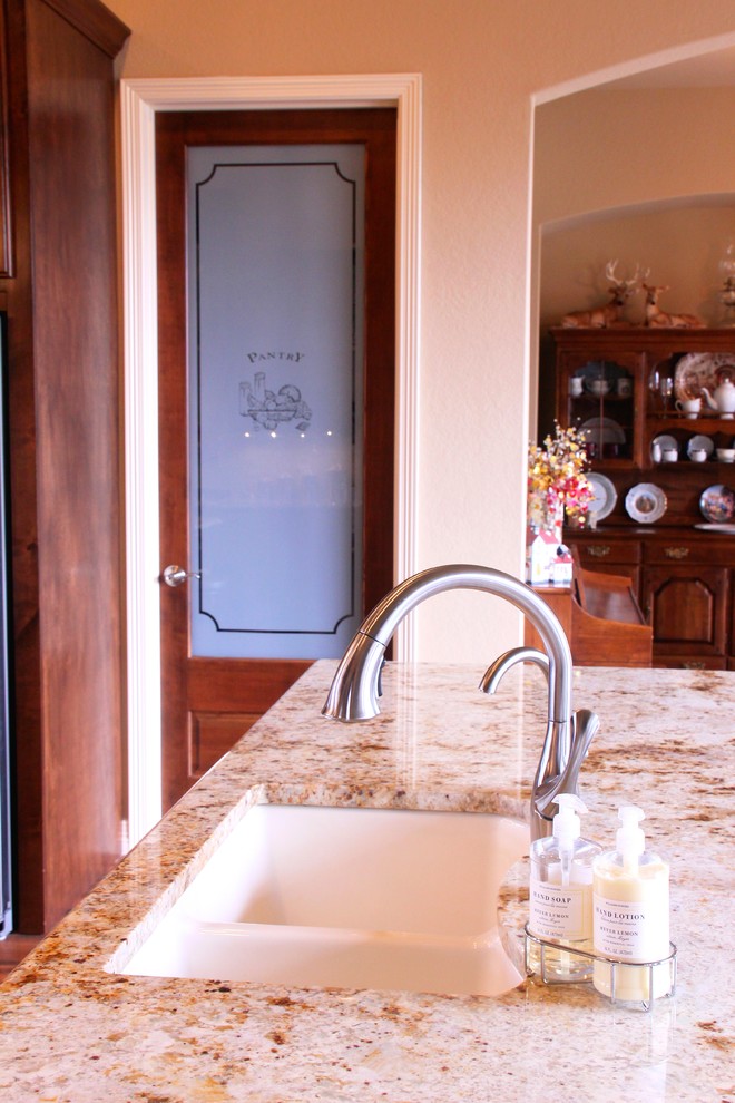 Example of a mid-sized mountain style u-shaped dark wood floor and brown floor enclosed kitchen design in Austin with an island, an undermount sink, raised-panel cabinets, dark wood cabinets, granite countertops, beige backsplash, stone tile backsplash and stainless steel appliances