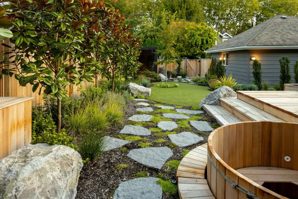 This is an example of a mid-sized transitional full sun backyard stone and wood fence landscaping in Vancouver with a fire pit for summer.