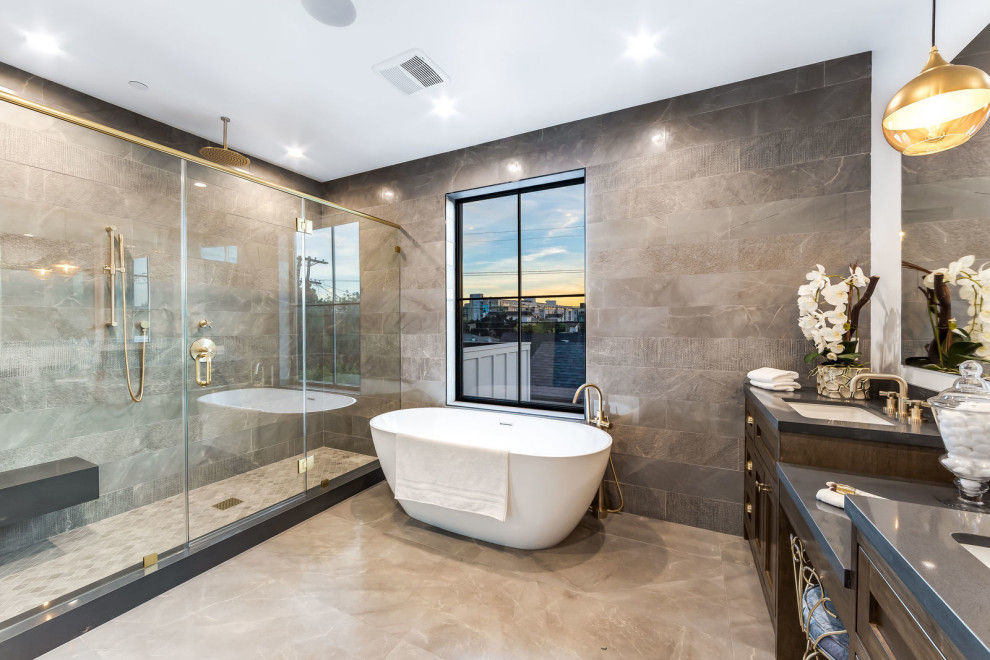 Inspiration for a large transitional master bathroom in Los Angeles with shaker cabinets, dark wood cabinets, a freestanding tub, gray tile, white walls, an undermount sink, a hinged shower door, grey benchtops, an alcove shower, a two-piece toilet, limestone, limestone floors, engineered quartz benchtops and grey floor.