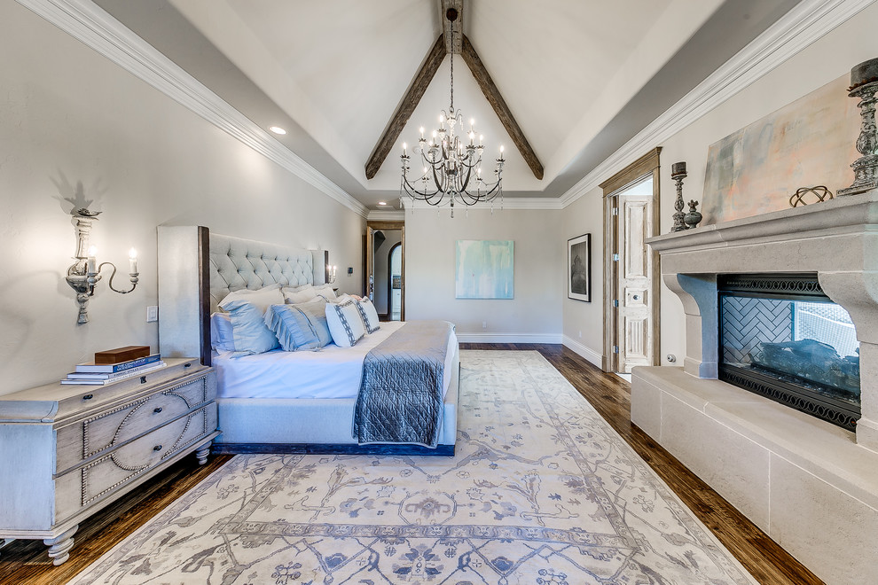 Large transitional master bedroom in Oklahoma City with grey walls, medium hardwood floors, a standard fireplace, a concrete fireplace surround and brown floor.