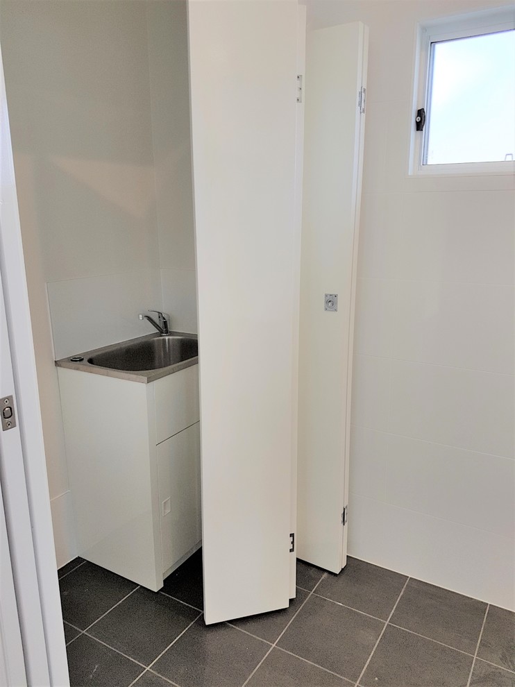 Photo of a small modern single-wall laundry cupboard in Sydney with a single-bowl sink, white cabinets, white walls and ceramic floors.