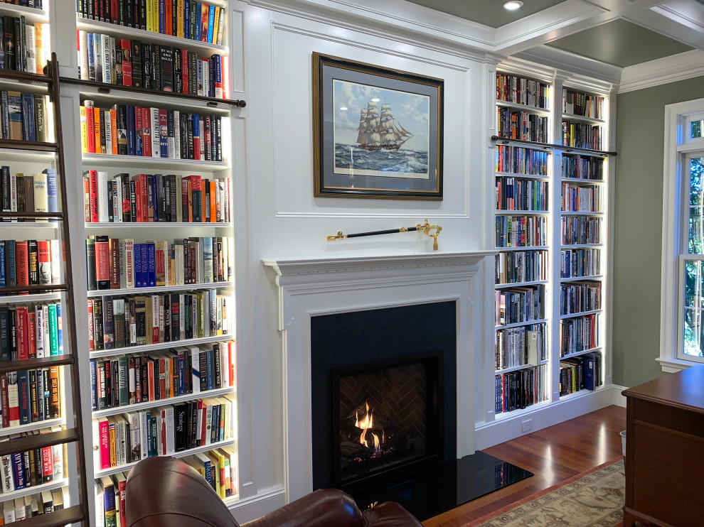 This is an example of a mid-sized traditional home office in Philadelphia with a library, green walls, medium hardwood floors, a standard fireplace, a wood fireplace surround, a freestanding desk, orange floor, coffered and panelled walls.