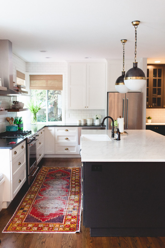 Photo of a transitional u-shaped kitchen in New York with a farmhouse sink, shaker cabinets, white cabinets, white splashback, subway tile splashback, stainless steel appliances, dark hardwood floors and with island.