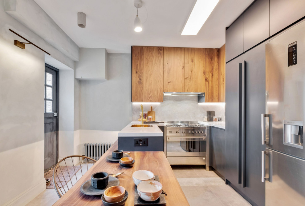 Photo of a mid-sized modern u-shaped eat-in kitchen in London with flat-panel cabinets, tile benchtops, grey splashback, porcelain splashback, stainless steel appliances, porcelain floors, a peninsula, grey floor, white benchtop, an integrated sink and black cabinets.