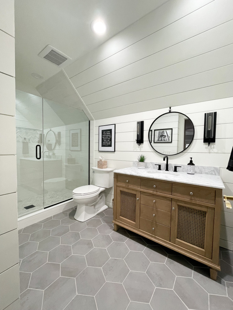 Photo of a mid-sized country kids bathroom in Detroit with recessed-panel cabinets, medium wood cabinets, an alcove shower, a two-piece toilet, white tile, porcelain tile, white walls, porcelain floors, an undermount sink, marble benchtops, grey floor, a hinged shower door, grey benchtops, a niche, a single vanity, a freestanding vanity, timber and planked wall panelling.