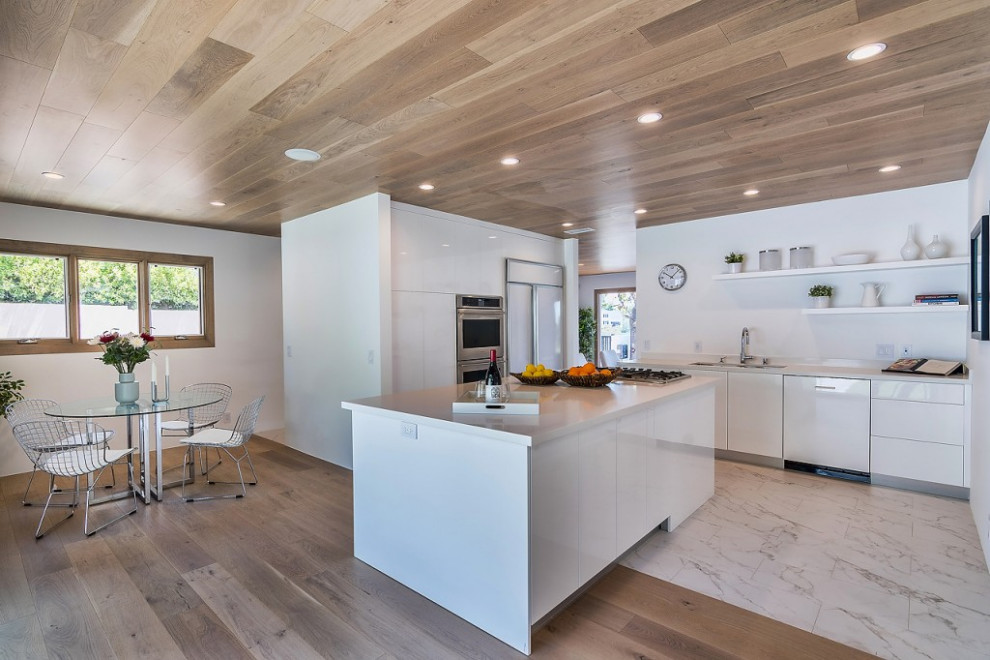 This is an example of a mid-sized midcentury l-shaped kitchen in Los Angeles with flat-panel cabinets, white cabinets, white splashback, with island, white floor and white benchtop.