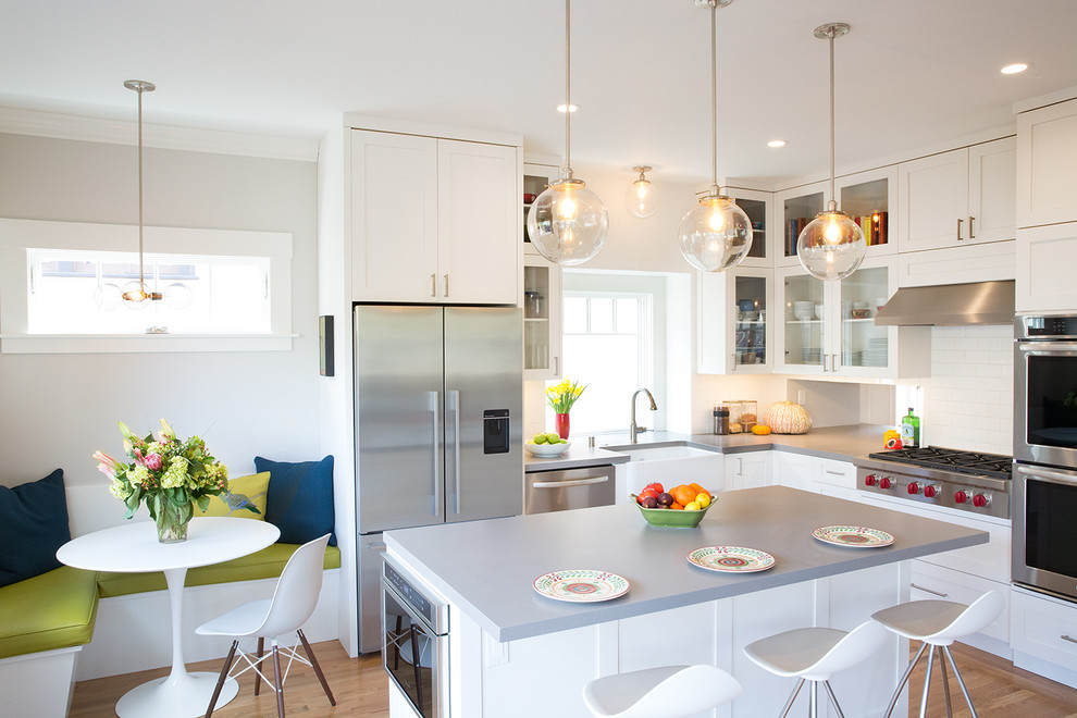 Photo of a transitional l-shaped eat-in kitchen in San Francisco with a farmhouse sink, shaker cabinets, white cabinets, white splashback, subway tile splashback, stainless steel appliances, light hardwood floors, with island and beige floor.