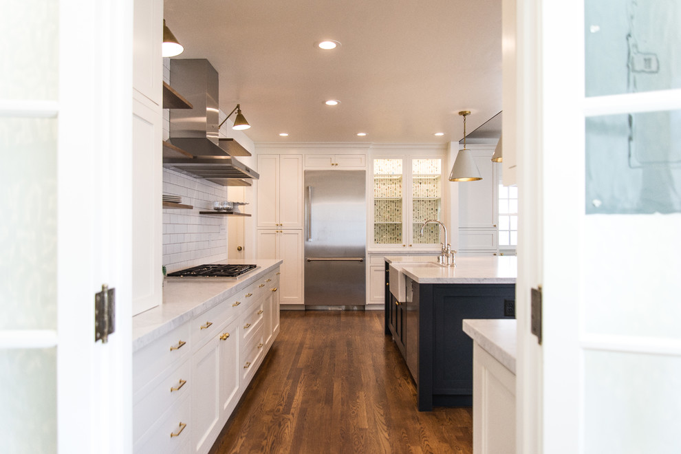 Photo of a large country u-shaped open plan kitchen in Sacramento with a farmhouse sink, shaker cabinets, white cabinets, marble benchtops, white splashback, subway tile splashback, stainless steel appliances, medium hardwood floors, with island, brown floor and white benchtop.