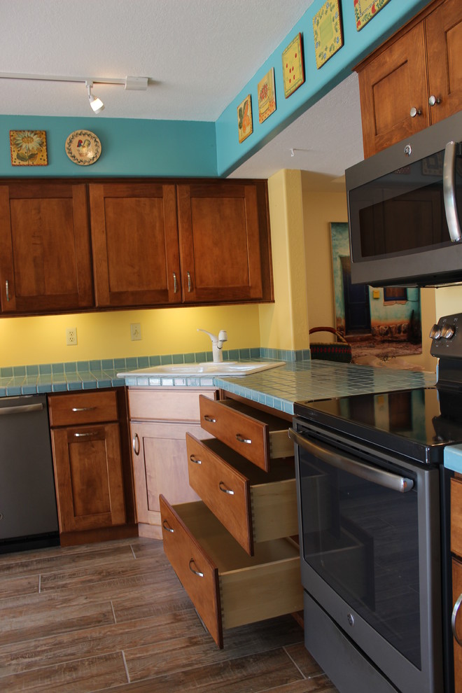 This is an example of a mid-sized arts and crafts l-shaped eat-in kitchen in Phoenix with a drop-in sink, recessed-panel cabinets, medium wood cabinets, tile benchtops, blue splashback, porcelain splashback, ceramic floors and no island.