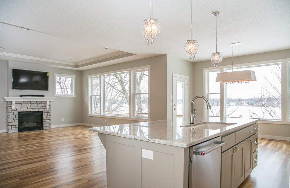 This is an example of a transitional l-shaped eat-in kitchen in Minneapolis with a drop-in sink, shaker cabinets, white cabinets, granite benchtops, grey splashback, ceramic splashback, stainless steel appliances, light hardwood floors and with island.