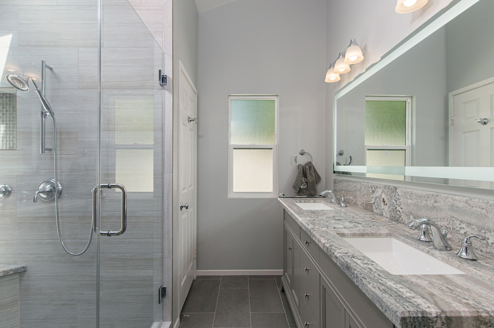 Photo of a large modern master bathroom in San Diego with recessed-panel cabinets, grey cabinets, an alcove tub, an open shower, a two-piece toilet, gray tile, porcelain tile, grey walls, porcelain floors, grey floor, a hinged shower door, an undermount sink, granite benchtops, grey benchtops, a double vanity and a built-in vanity.