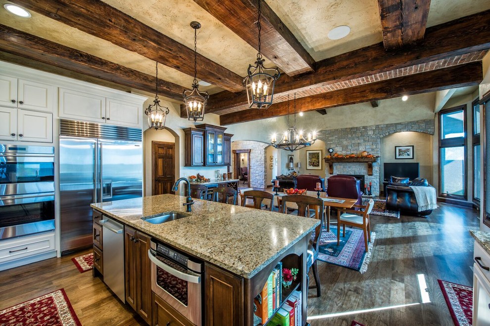 Open concept kitchen - huge rustic u-shaped dark wood floor open concept kitchen idea with an undermount sink, beaded inset cabinets, white cabinets, granite countertops, white backsplash, stainless steel appliances and an island