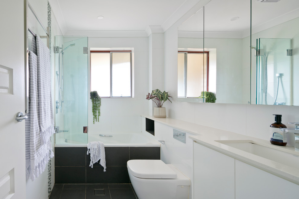Photo of a contemporary bathroom in Sydney with a drop-in tub, a shower/bathtub combo, a wall-mount toilet, white tile, white walls, ceramic floors, an undermount sink, engineered quartz benchtops, grey floor and a hinged shower door.