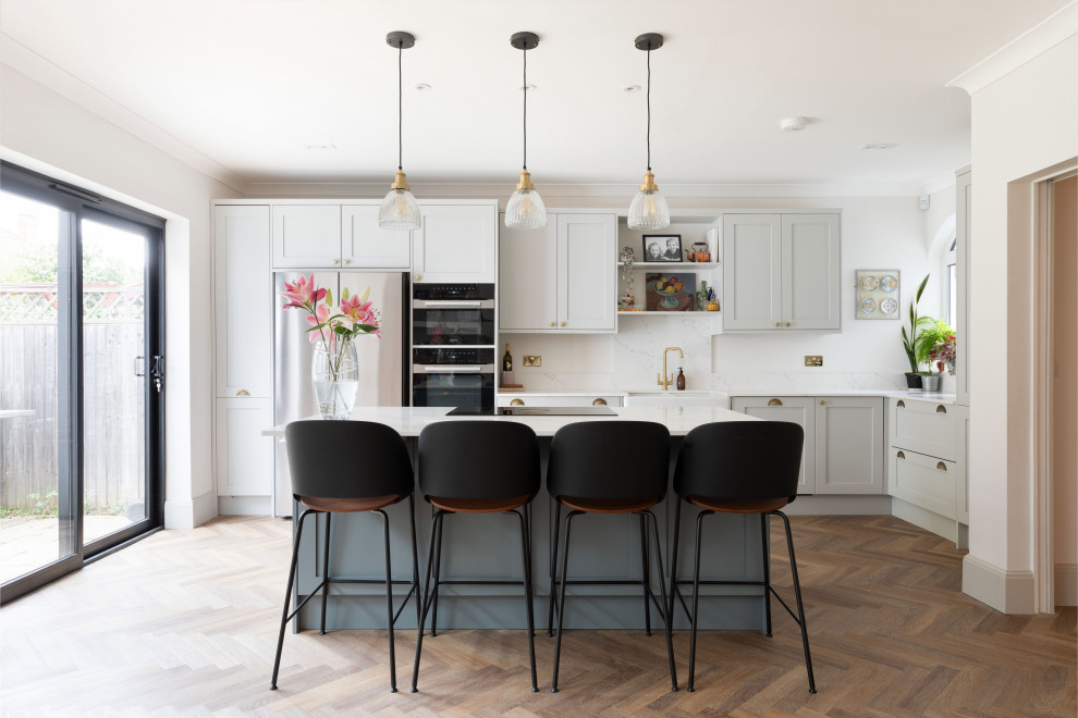 Klassische Küche in L-Form mit Landhausspüle, Schrankfronten im Shaker-Stil, grauen Schränken, Küchengeräten aus Edelstahl, dunklem Holzboden, Kücheninsel, braunem Boden und weißer Arbeitsplatte in London