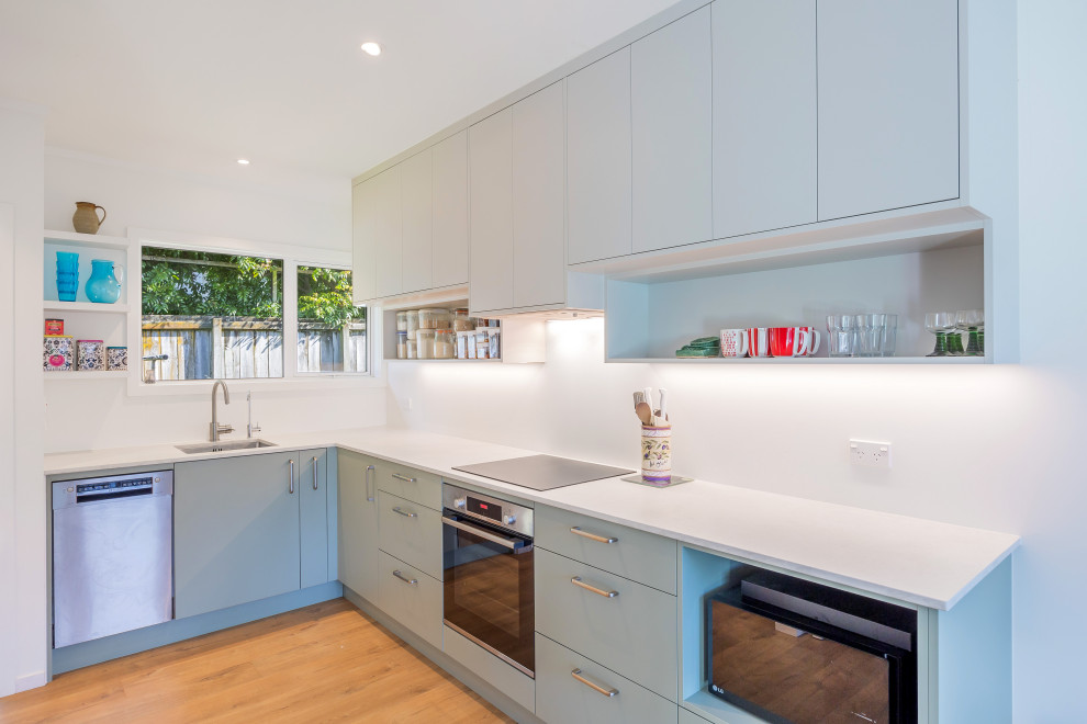 Small trendy l-shaped laminate floor and brown floor eat-in kitchen photo in Auckland with an undermount sink, flat-panel cabinets, green cabinets, quartz countertops, white backsplash, stainless steel appliances, no island and white countertops