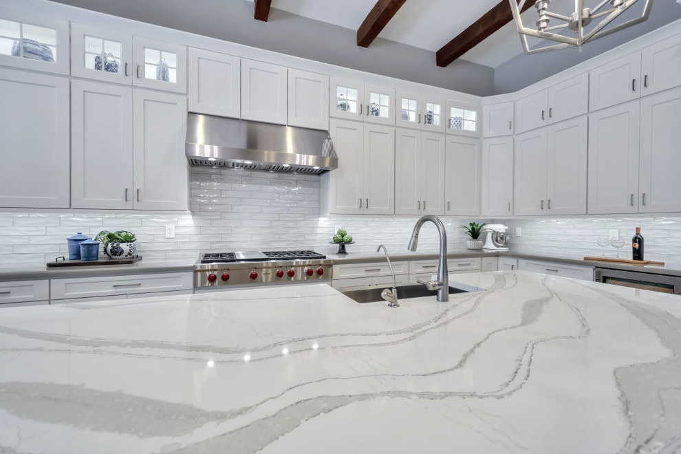 Example of a large transitional u-shaped porcelain tile, beige floor and exposed beam enclosed kitchen design in Phoenix with a farmhouse sink, shaker cabinets, white cabinets, quartz countertops, white backsplash, glass tile backsplash, stainless steel appliances, an island and white countertops