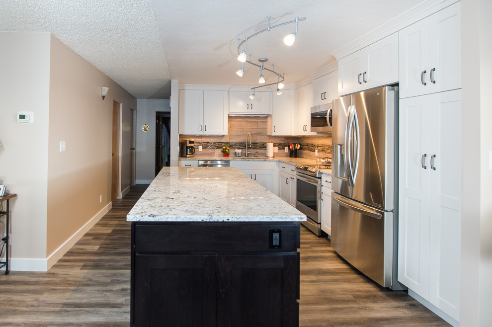 Example of a small transitional l-shaped brown floor and laminate floor open concept kitchen design with an undermount sink, shaker cabinets, white cabinets, granite countertops, beige backsplash, matchstick tile backsplash, stainless steel appliances and an island