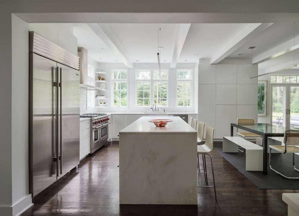 Photo of a large modern l-shaped eat-in kitchen in New York with flat-panel cabinets, white cabinets, solid surface benchtops, white splashback, stone slab splashback, stainless steel appliances, dark hardwood floors and with island.