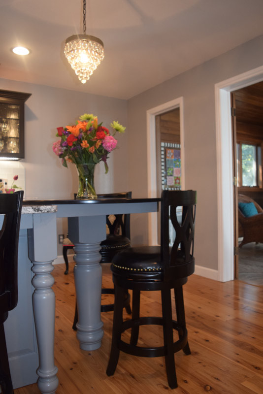 Example of a transitional medium tone wood floor kitchen design in Chicago with a farmhouse sink, raised-panel cabinets, black cabinets, quartz countertops, white backsplash, glass tile backsplash, stainless steel appliances and an island
