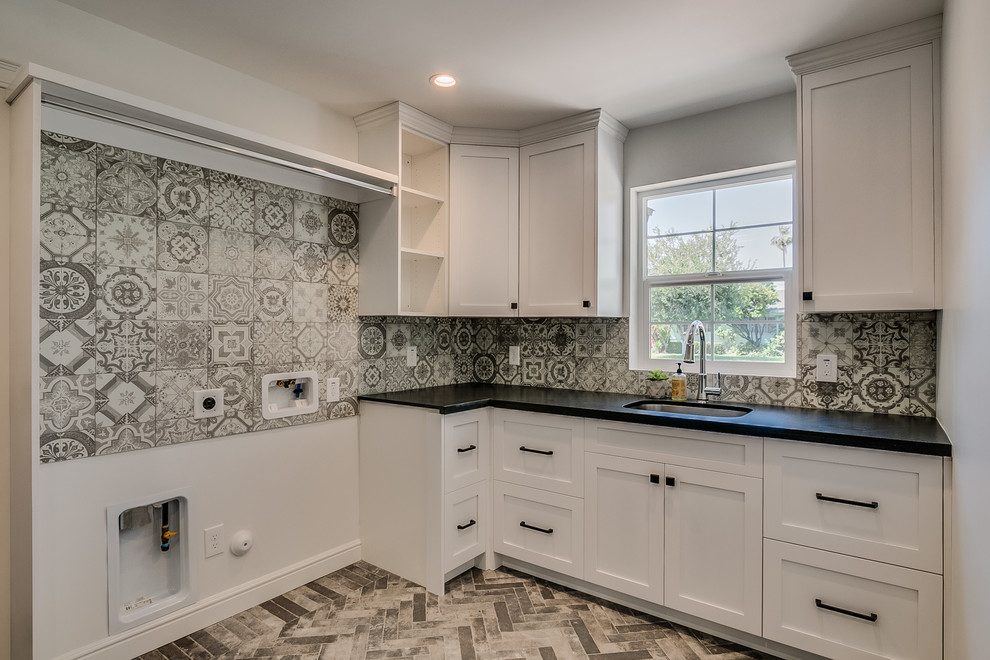 Inspiration for a large country l-shaped dedicated laundry room in Phoenix with an undermount sink, recessed-panel cabinets, white cabinets, granite benchtops, white walls, ceramic floors, a side-by-side washer and dryer, grey floor and black benchtop.