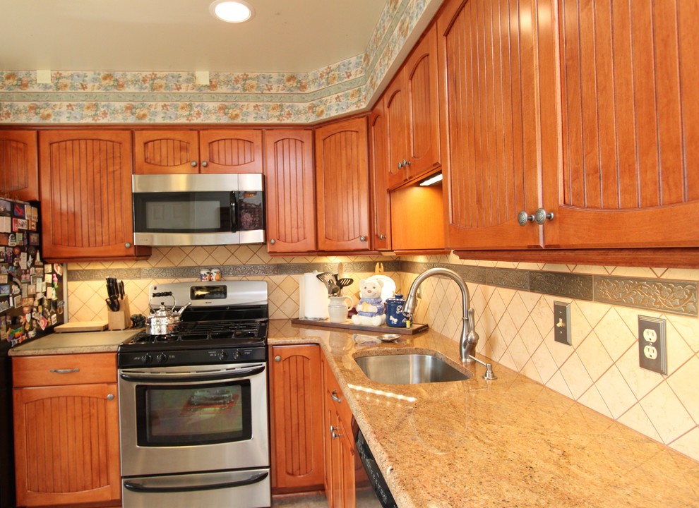Photo of a country l-shaped kitchen in Baltimore with an undermount sink, beaded inset cabinets, medium wood cabinets, granite benchtops, beige splashback, ceramic splashback, stainless steel appliances, linoleum floors and no island.